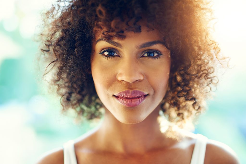 Portrait of perfect afro-american woman looking at camera with semi-smile on blurred background.